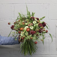 a man is holding a bouquet of red and green flowers